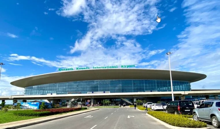 Modern airport terminal building with distinctive curved design under blue sky with white clouds and parked vehicles in foreground